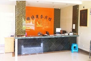 Un comptoir d’accueil avec un plateau en marbre noir, un tabouret bleu et un mur orné d’un motif et de caractères chinois.