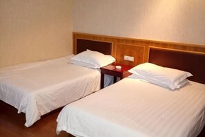 Deux lits simples avec des têtes de lit en bois, une table de chevet avec une lampe et une prise électrique murale.