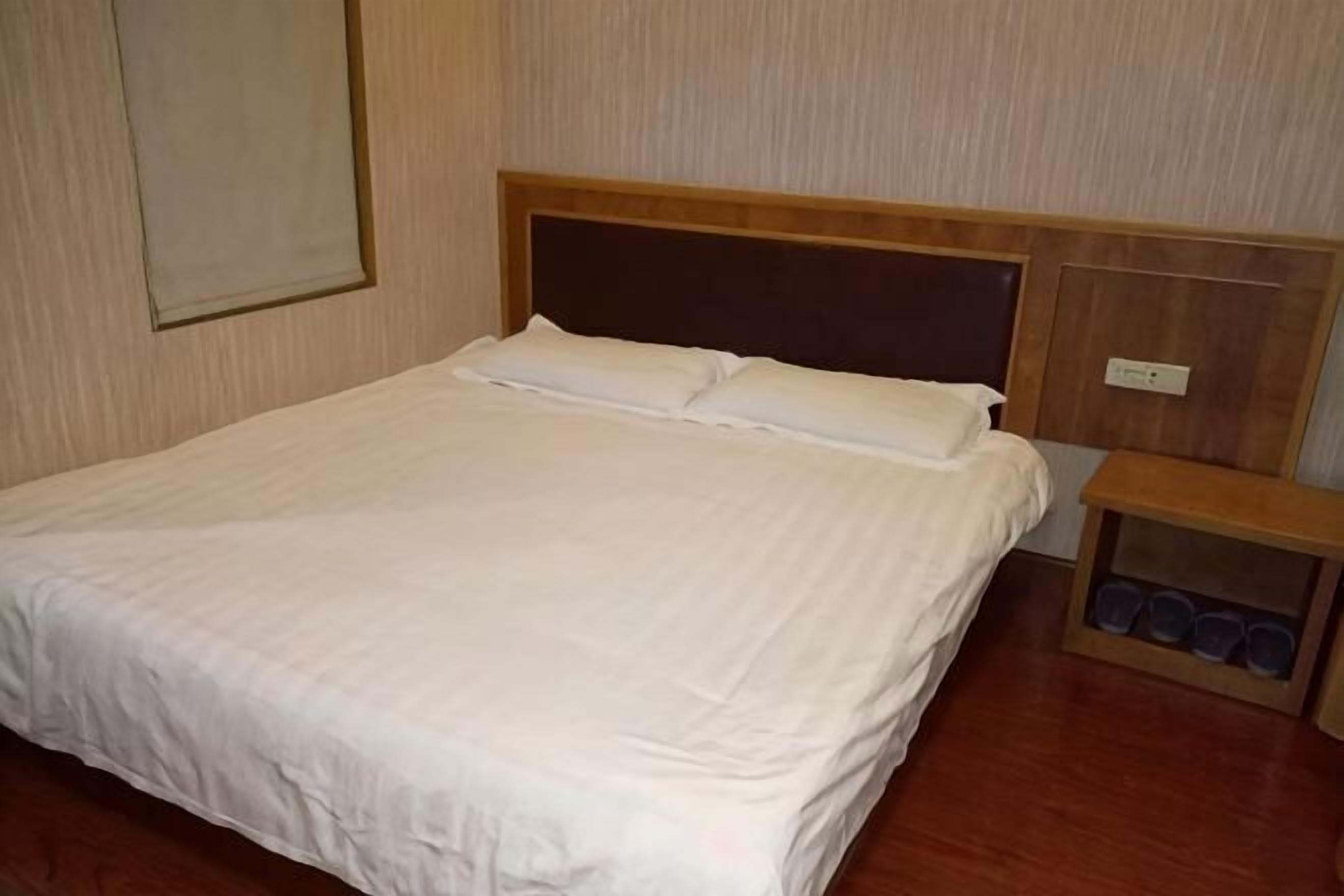 A neatly made bed with a wooden headboard, a bedside table with cups, and a wall-mounted light switch.