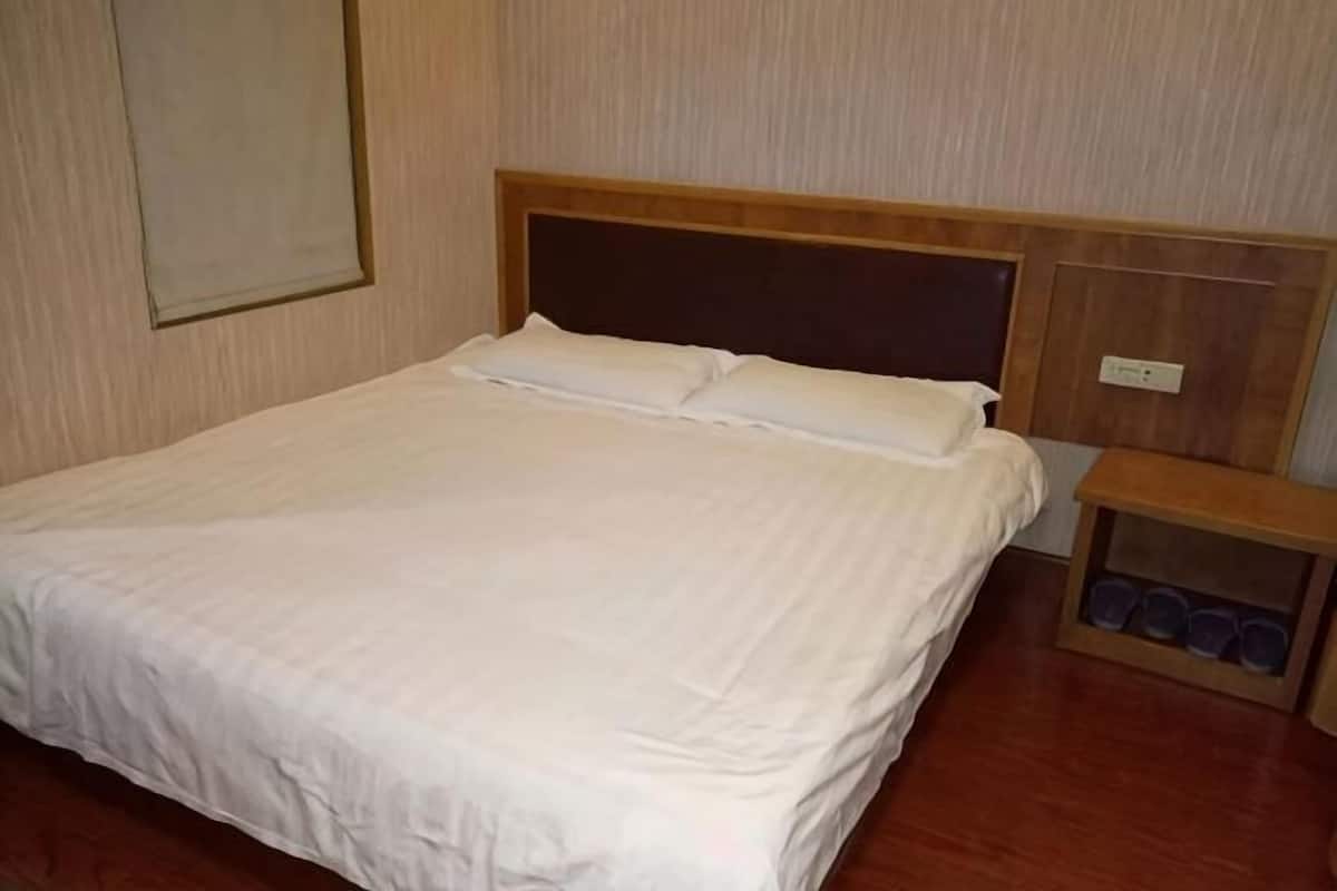 A neatly made bed with a wooden headboard, a bedside table with cups, and a wall-mounted light switch.