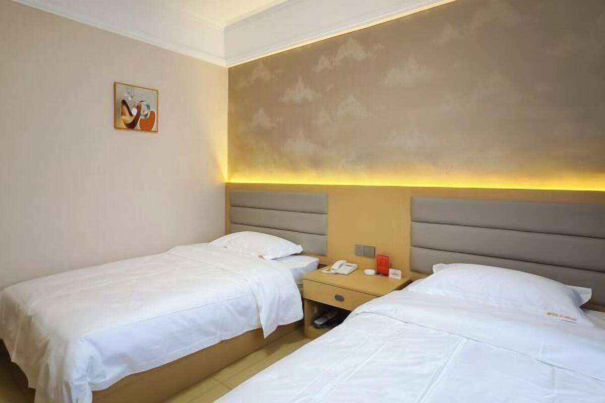 A hotel room with two beds, a bedside table with a phone and a red object, and a wall-mounted artwork.