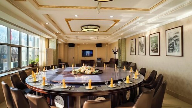 A conference room with a round table, chairs, a television, and framed artwork on the walls. - Donggang Yuyun Hotel (Donggang)