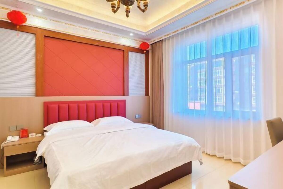 A hotel room with a large bed, a nightstand, a desk, and a window with curtains.