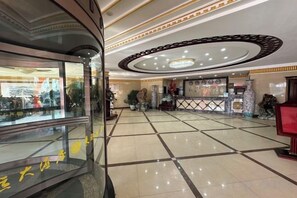 Un hall d’hôtel avec un comptoir d’accueil, un grand vase et une vitrine.