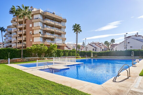 Une piscine avec un plongeoir, entourée d’une pelouse et bordée d’un immeuble à plusieurs étages doté de balcons.