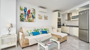 A modern living room with a sofa, coffee table, and kitchen area with appliances.
