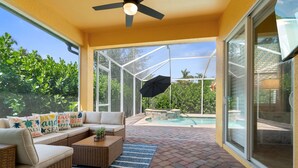 Un patio cubierto con un sofá, una mesa de centro y una piscina al fondo.