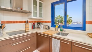 Cozinha moderna com uma grande janela, eletrodomésticos de aço inoxidável e vista para o mar.