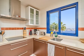 Een moderne keuken met een groot raam, roestvrijstalen apparatuur en uitzicht op zee.