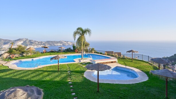 Piscina com vista para o mar, rodeada por relva e guarda-sóis.