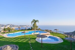 A swimming pool with a view of the sea, surrounded by grass and umbrellas. - Holiday Home 'Los Altos 23' with Sea View, Wi-Fi and Air Conditioning (Almuñécar)