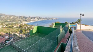 Terraço com quadra de tênis, piscina e vista para a costa.