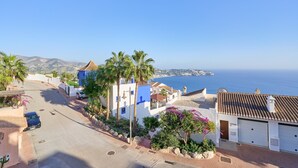 Uma rua costeira com edifícios, um carro estacionado e vista para o mar.