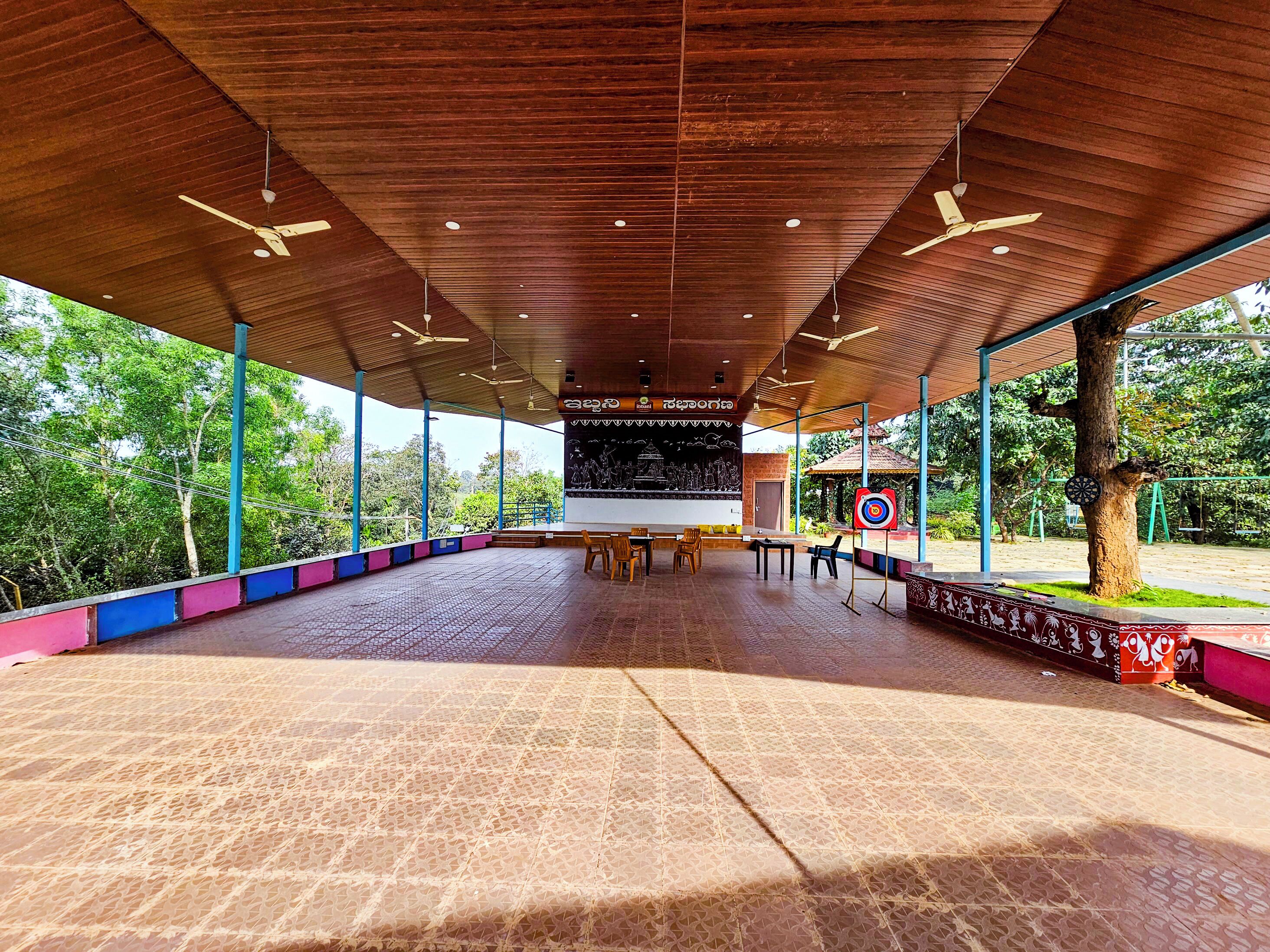 An open pavilion with a tiled floor, ceiling fans, and a large blackboard with writing.