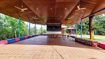 An open pavilion with a tiled floor, ceiling fans, and a large blackboard with writing.