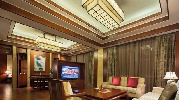 A hotel room with a wooden floor, a television, a sofa, a dining table, and a ceiling with recessed lighting. - Ji'an Hotel (Ji'an)