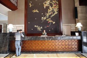 A reception desk with a large decorative wall mural, a wooden panel design, and two lamps. - Ji'an Hotel (Ji'an)