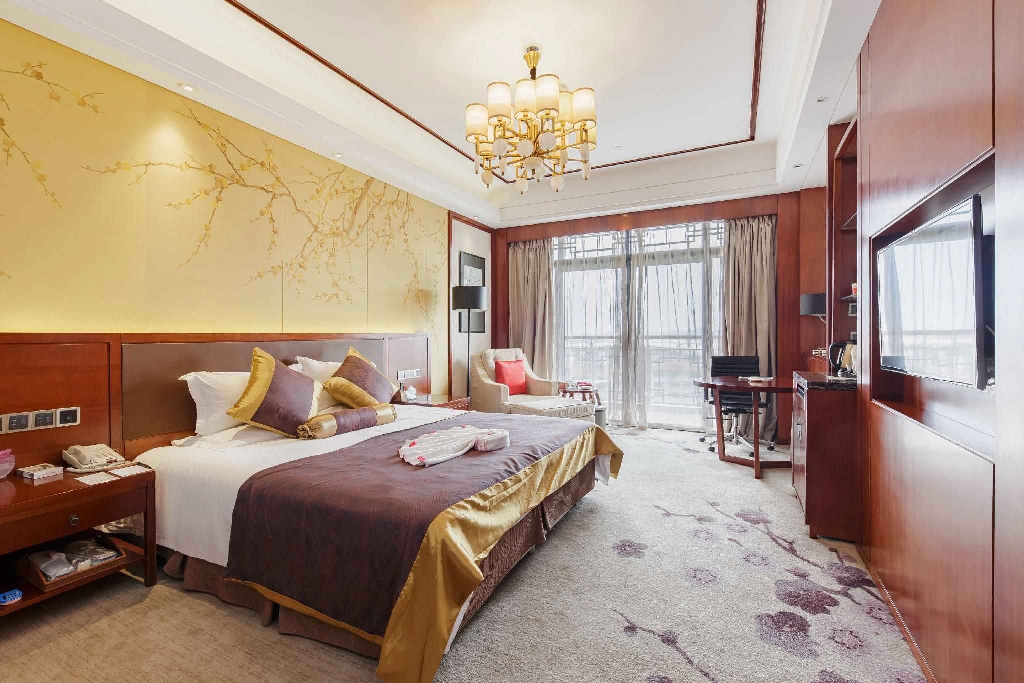 Quarto de hotel com cama grande, mesa de cabeceira, abajur e vista para o exterior pela janela.