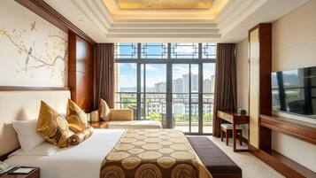 A hotel room with a large bed, a desk, a TV, and a view of the city.