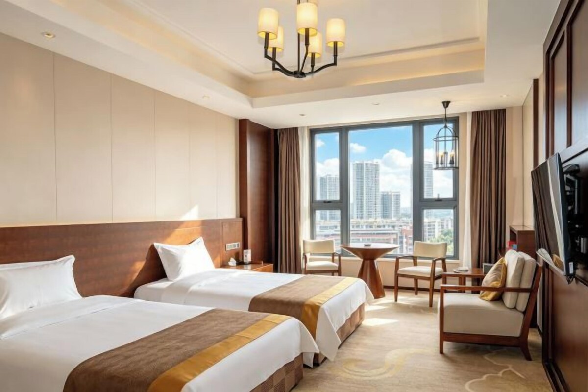 A hotel room with two beds, a TV, a city view, and a small table with chairs.