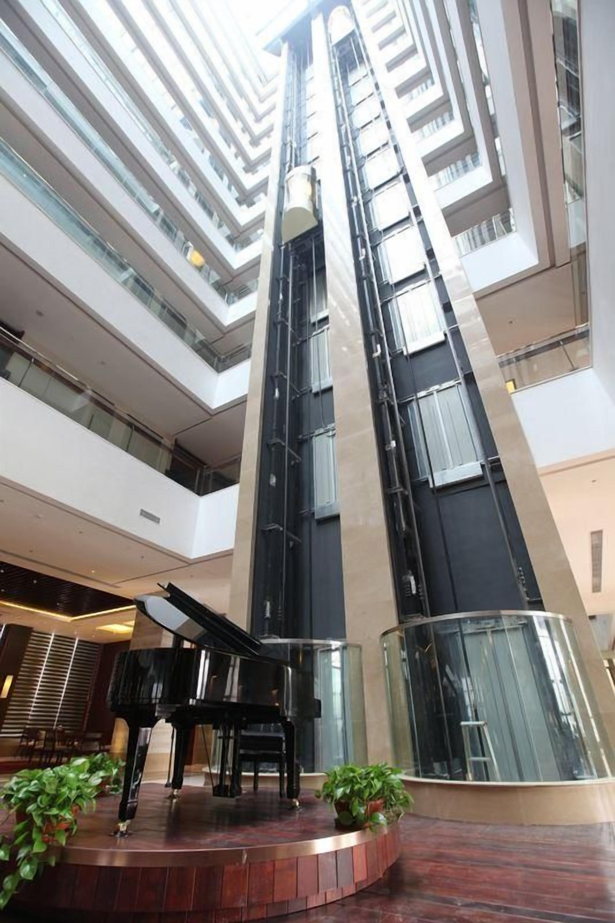 A multi-level atrium with a grand piano on a circular stage, surrounded by potted plants.