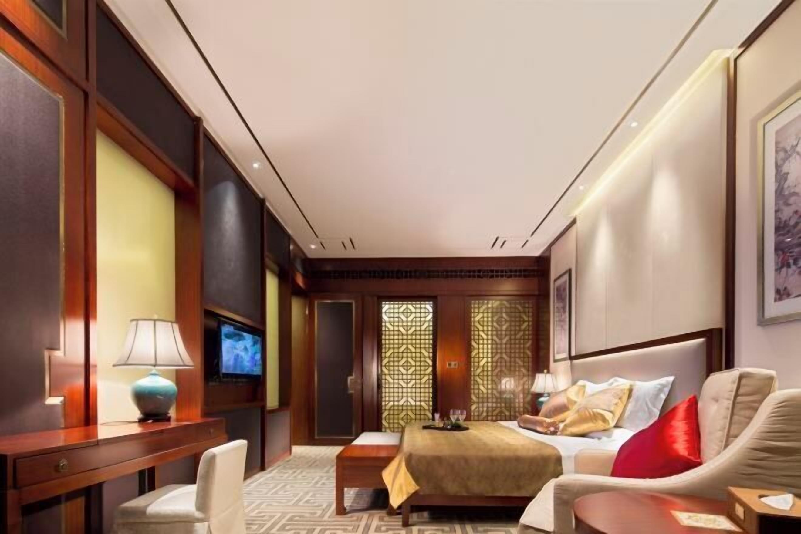 A hotel room with a bed, a desk with a lamp, a TV, and a decorative screen.