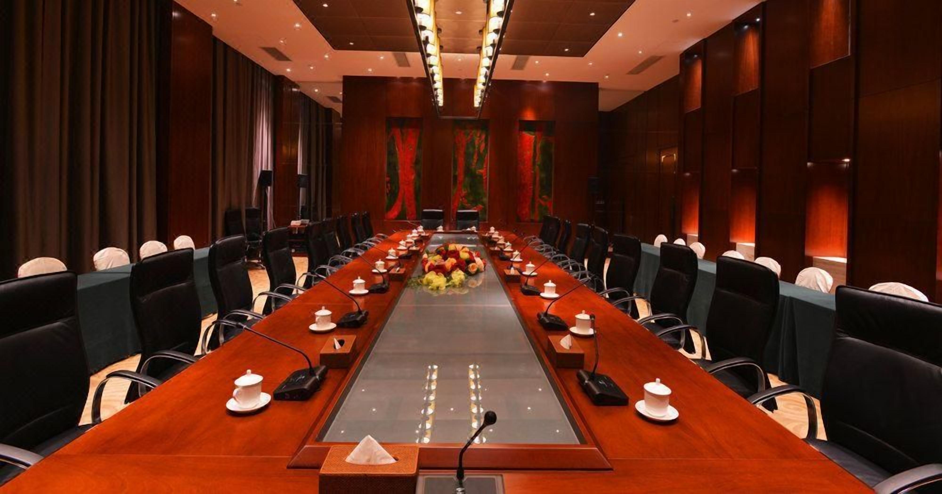 Un salón de conferencias con una larga mesa, sillas, micrófonos y un atril.