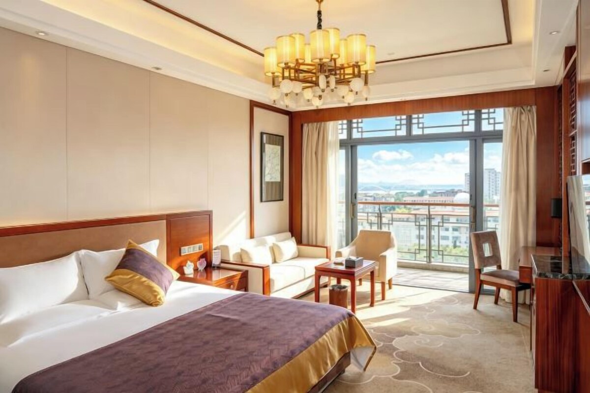 A hotel room with a large bed, a sofa, a desk, and a view of the city.