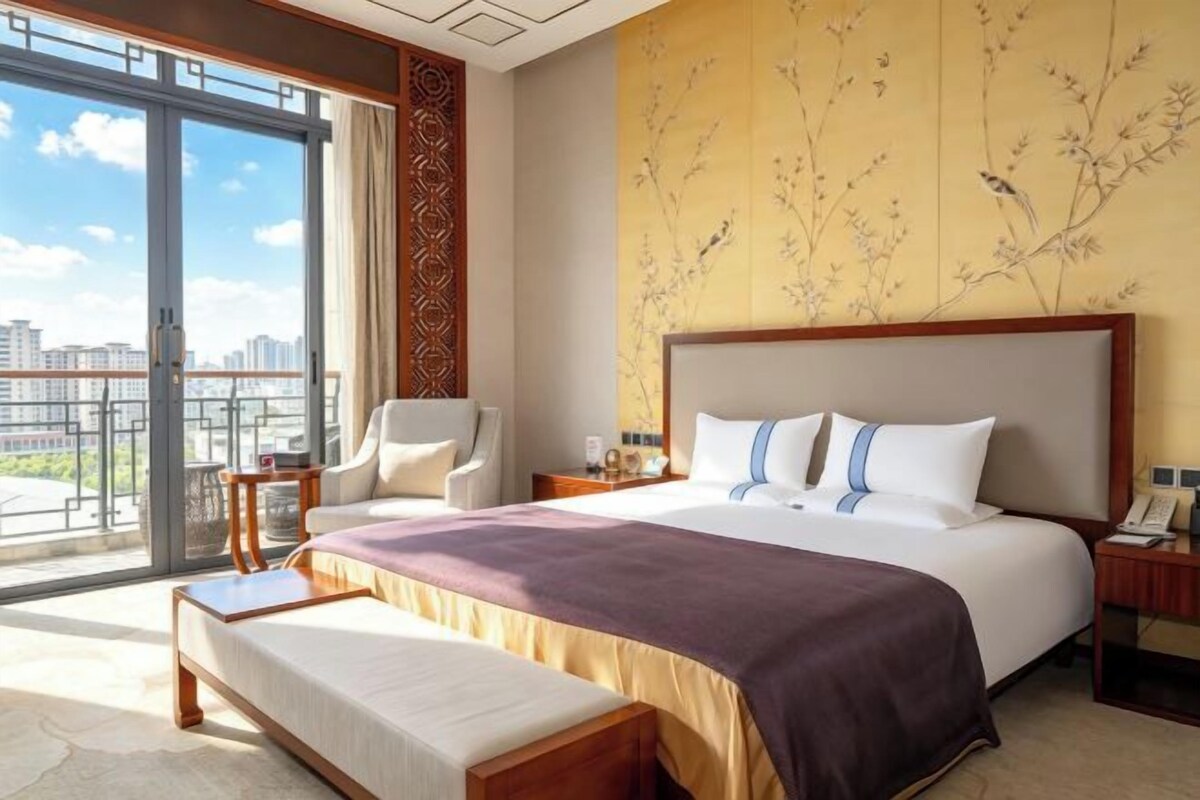 A hotel room with a large bed, a chair, a desk, and a view of the city.