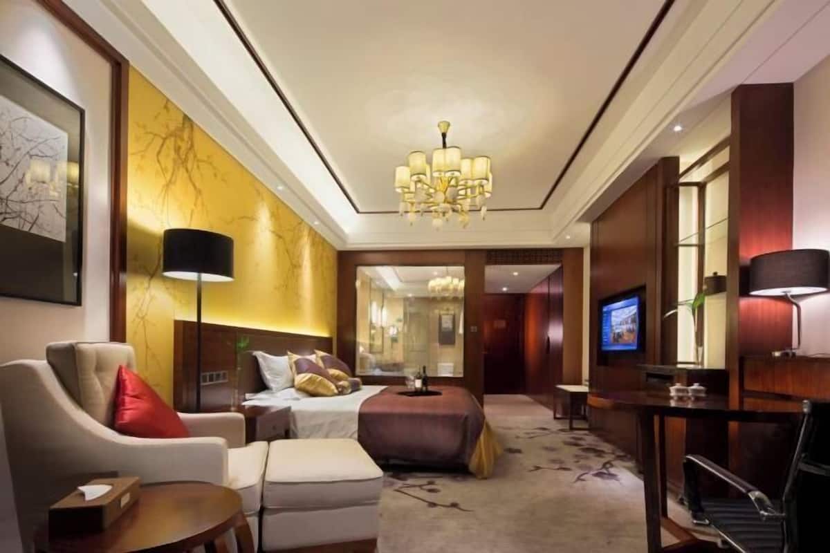 Ein Hotelzimmer mit Bett, Sofa, Schreibtisch, Fernseher und einer Chandelier.