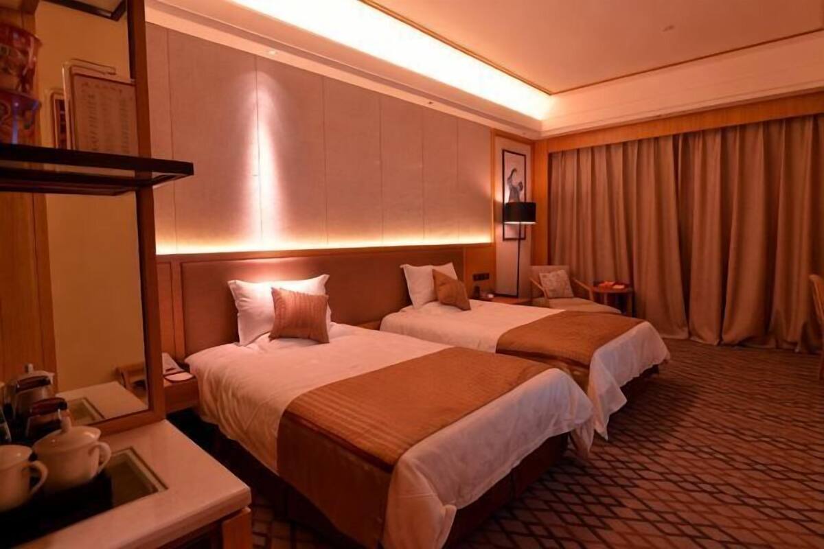 Ein Hotelzimmer mit zwei Betten, einem Nachttisch, einer Lampe und einem Fenster mit Vorhängen.