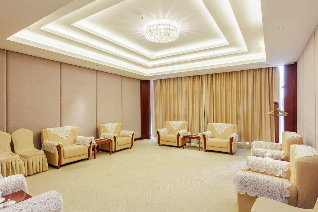 A hotel room with a large seating area, a chandelier, and a large window with curtains.