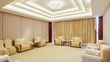 A hotel room with a large seating area, a chandelier, and a large window with curtains.