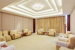 Habitación de hotel con un amplio espacio de estar, un candelabro y un ventanal con cortinas.