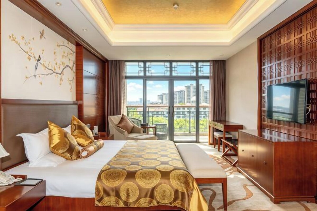 A hotel room with a large bed, a TV, a desk, and a view of the city.