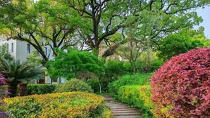 A wooden pathway leading through a lush garden with various green and yellow plants, surrounded by trees and a building in the background. - Ji'an Hotel (Ji'an)