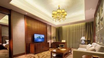 Una habitación de hotel con televisión, mueble de entretenimiento de madera, sofá, mesa de centro y candelabro.