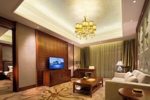 A hotel room with a television, a wooden entertainment unit, a sofa, a coffee table, and a chandelier. - Ji'an Hotel (Ji'an)