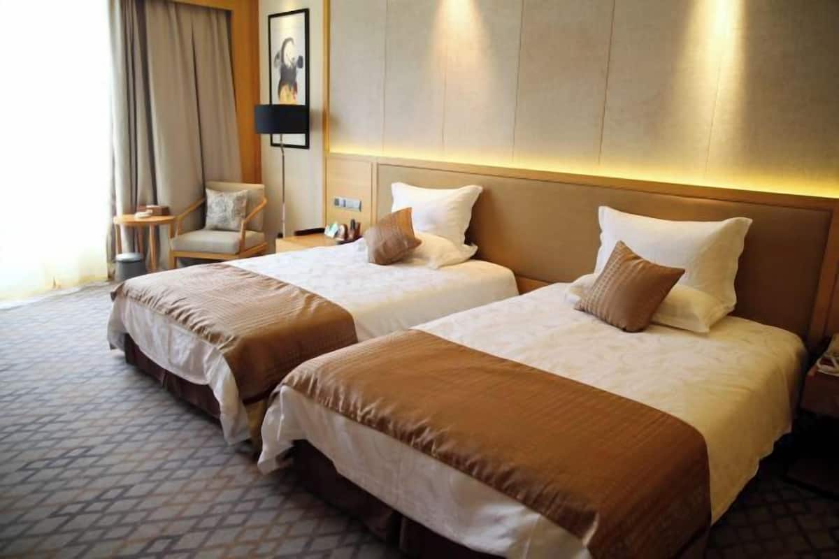 Ein Hotelzimmer mit zwei Betten, einem Sessel, einer Lampe und einem Bild an der Wand.