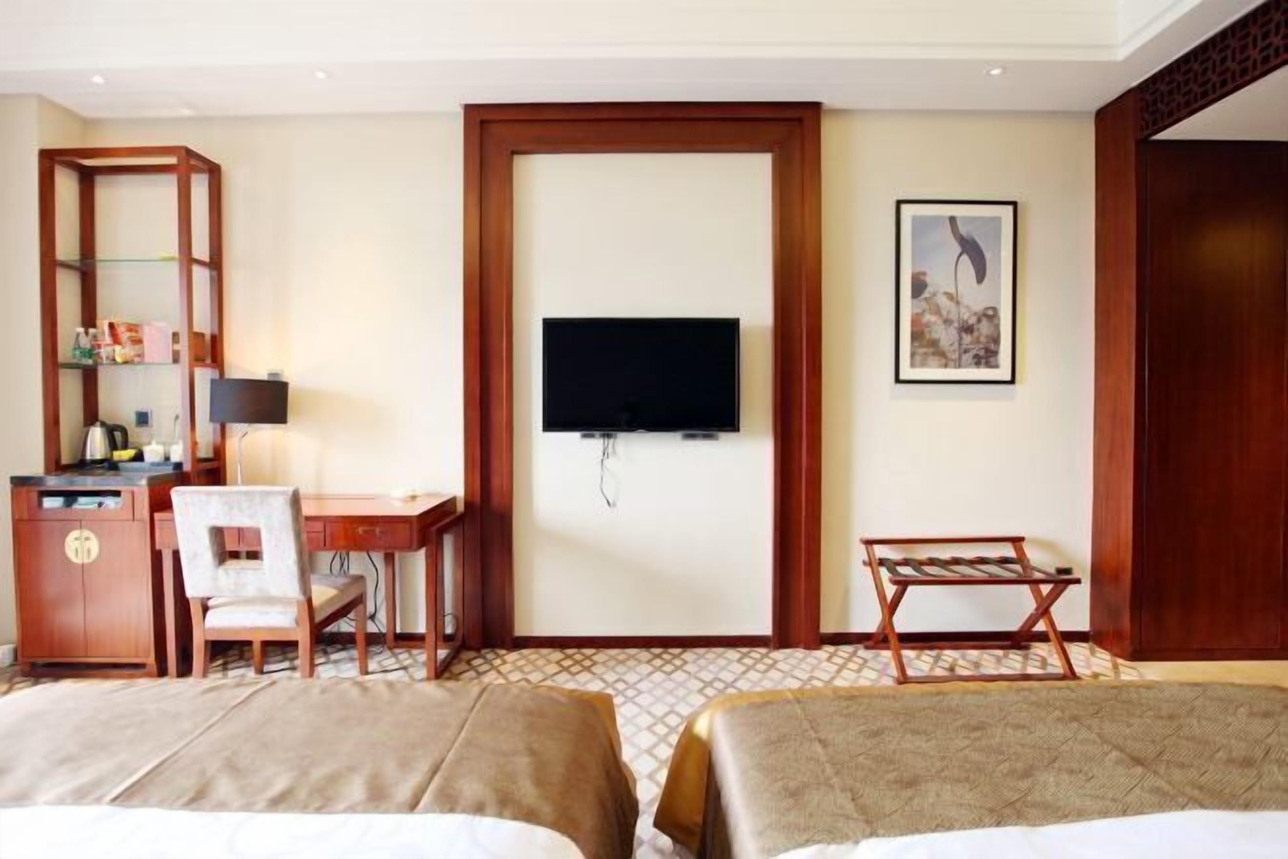 A hotel room with two beds, a desk with a chair, a television, a bookshelf, and a framed picture on the wall.