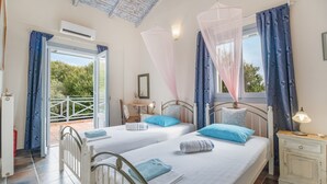 A bedroom with two beds, a bedside table, a nightstand, a window with curtains, and an air conditioning unit. - Villa Simeoni Country House with Lake View, Wi-Fi, and Air Conditioning (Lefkada Town)