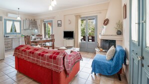 A cozy living room with a red sofa, a blue armchair, a fireplace, and a dining area with a table and chairs. - Villa Simeoni Country House with Lake View, Wi-Fi, and Air Conditioning (Lefkada Town)