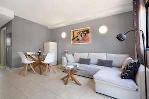 A modern living room with a sofa, a glass coffee table, a dining table with chairs, a painting on the wall, and a lamp. - Vacation Home 'Oasis Royal E204' with Shared Pool, Shared Terrace and Wi-Fi (Corralejo)
