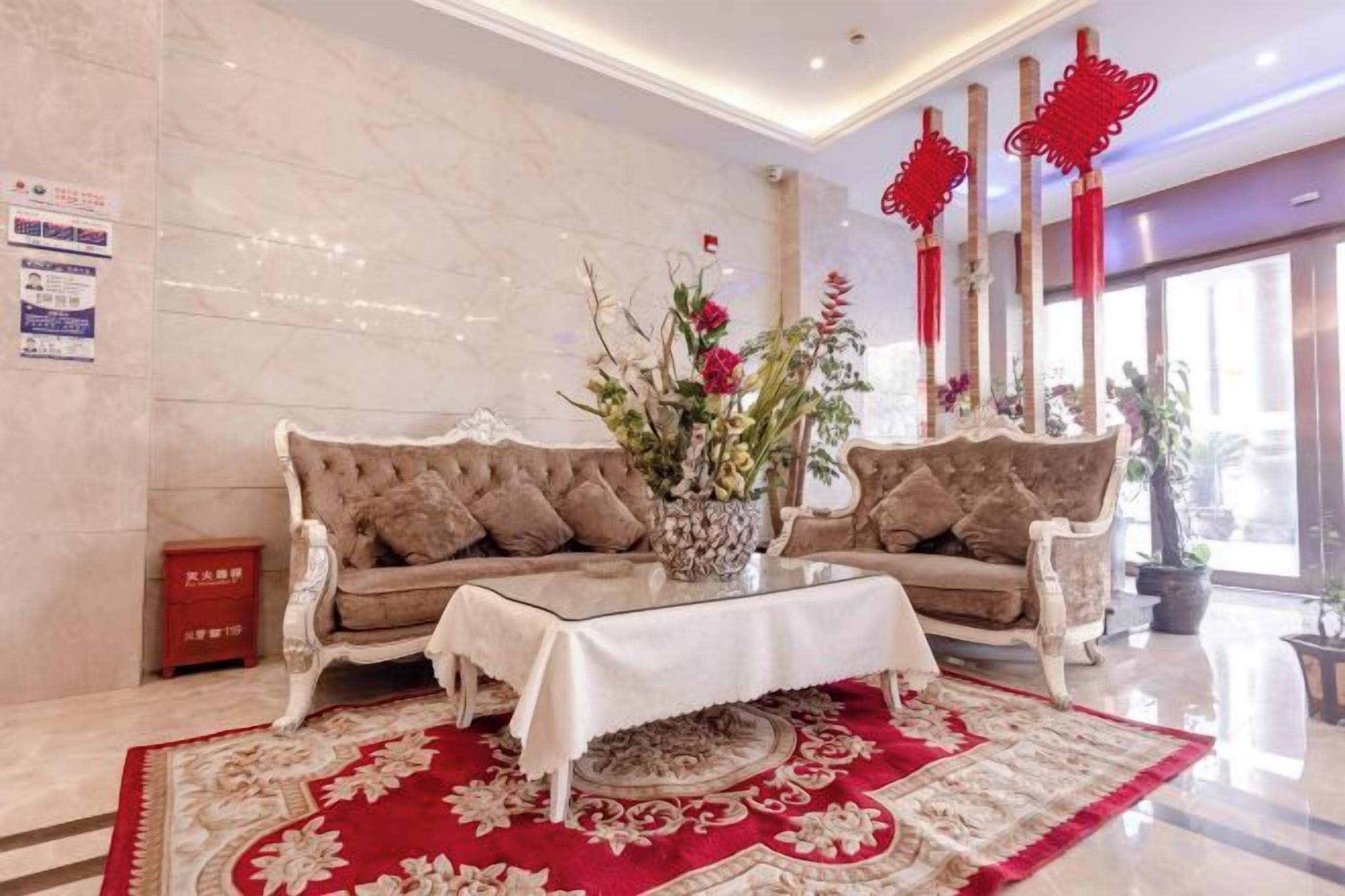 Vestíbulo de hotel con pared de mármol, dos sofás, una mesa de centro y detalles decorativos rojos.