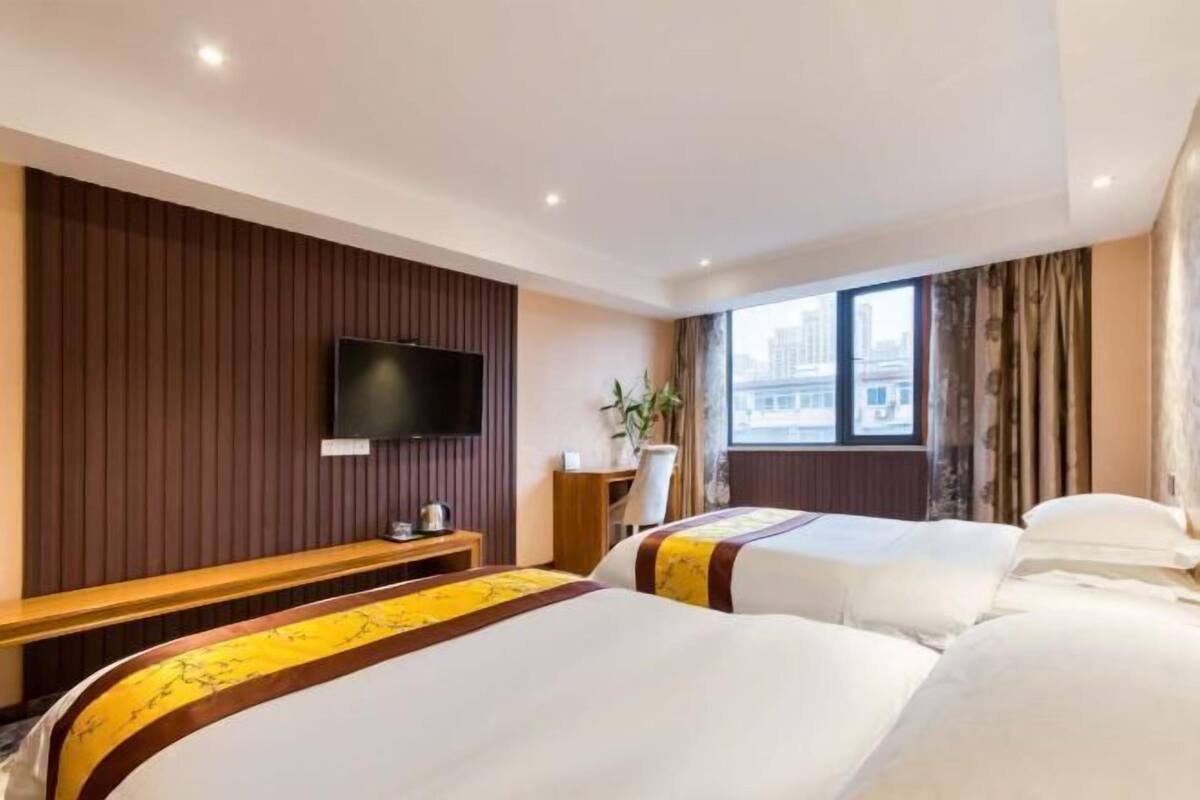 Una camera d'albergo con due letti, una televisione, una scrivania e una finestra vista città.