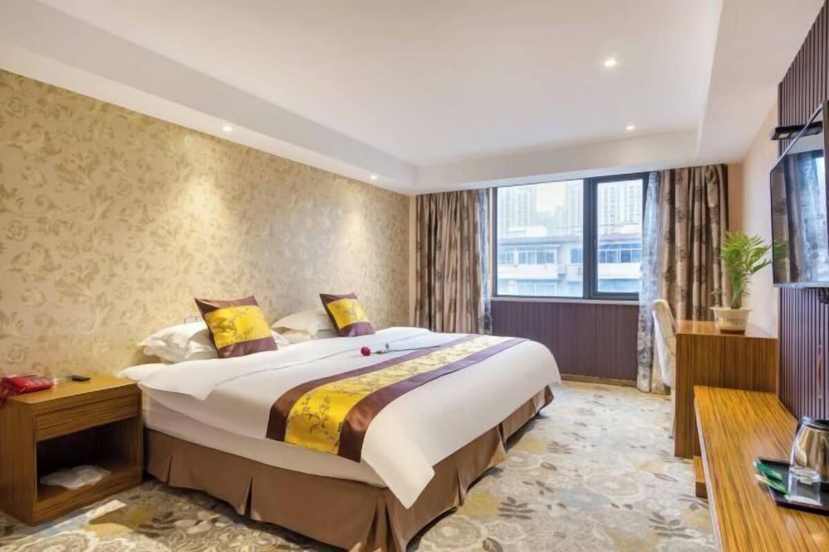 Camera d'albergo con un letto grande, un comodino in legno, una scrivania e una finestra con tende.