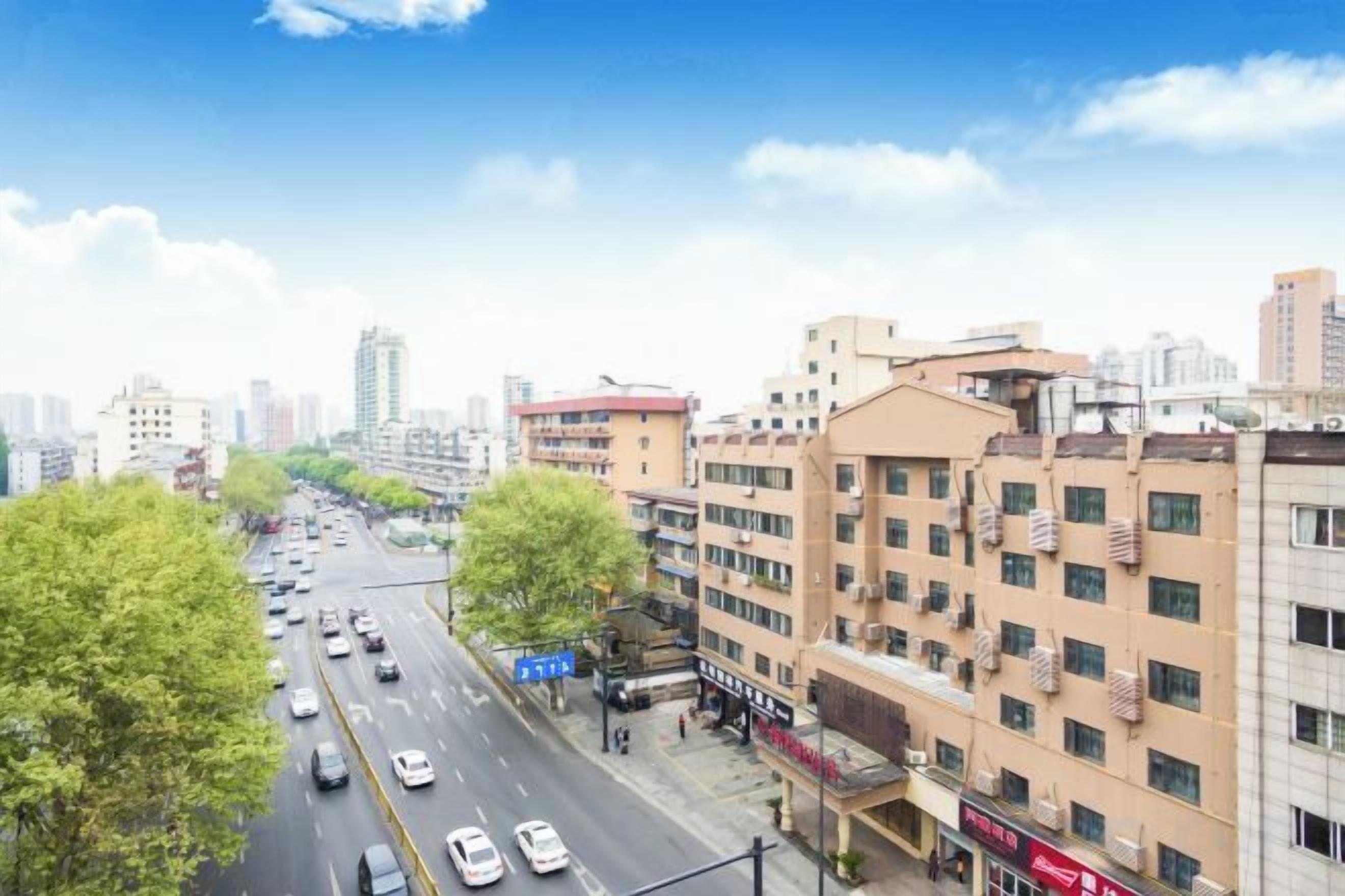 Un edificio de varios pisos con una fila de tiendas en la planta baja, cielo despejado y una calle concurrida con coches.