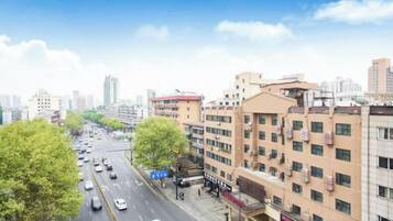Un edificio de varios pisos con una fila de tiendas en la planta baja, cielo despejado y una calle concurrida con coches.