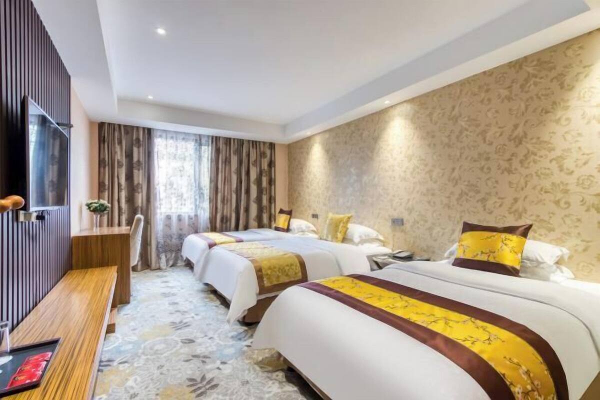 Una camera d'albergo con due letti, una panca in legno, una TV e un tappeto decorato.