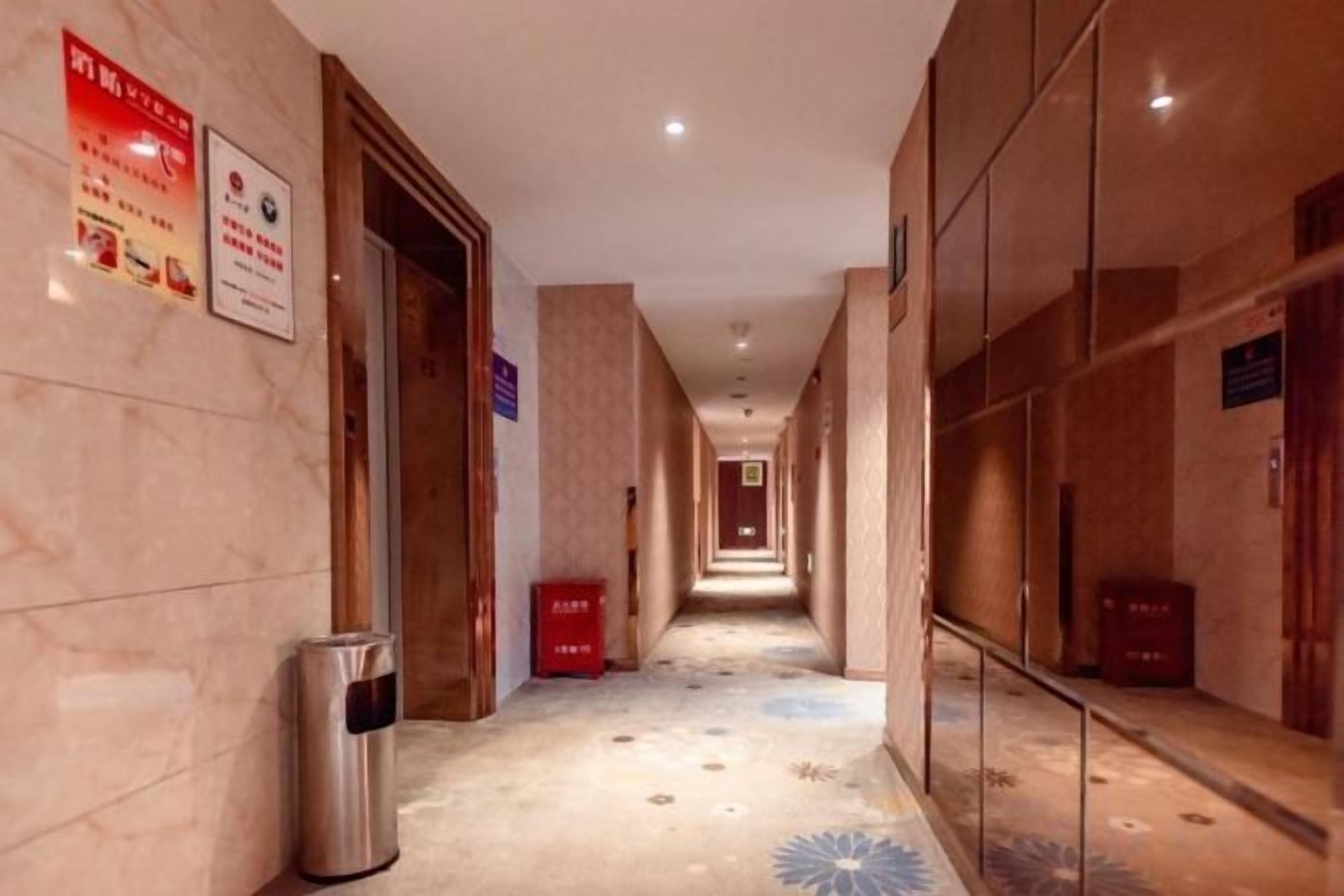 A hotel corridor with a trash bin, a red box, and directional signs on the walls.